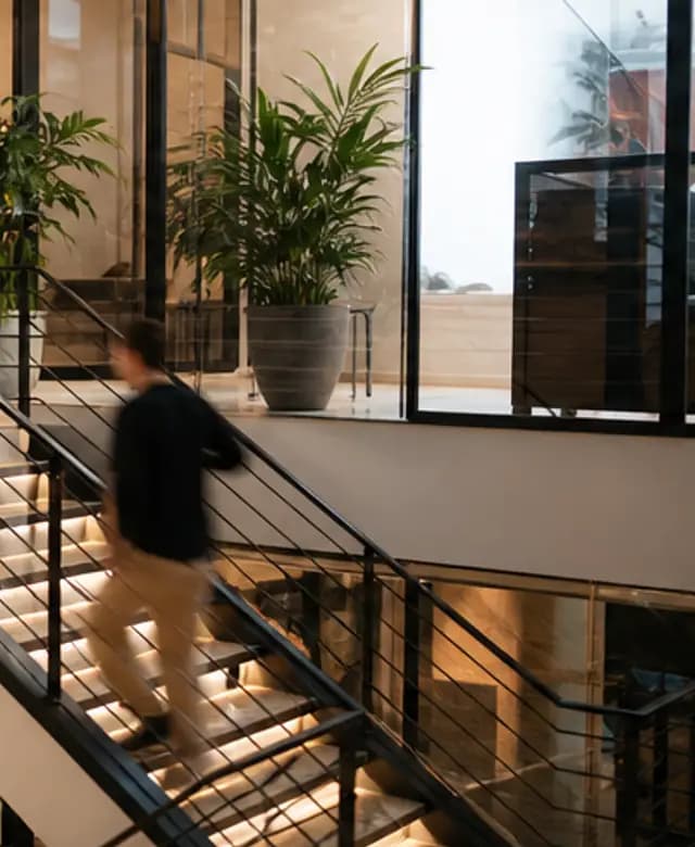 A warm glass-and-wood studio stair with a teammate in motion